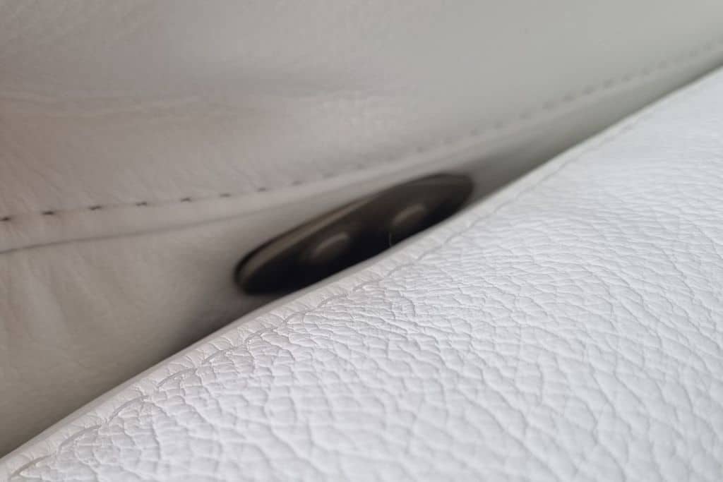 Bílá kožená sedací souprava detail ukrytí polohovacího tlačítka na sedacím polštáři. 